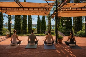 Vier personen mediteren op yogamatten onder een pergola, met een prachtig uitzicht.
