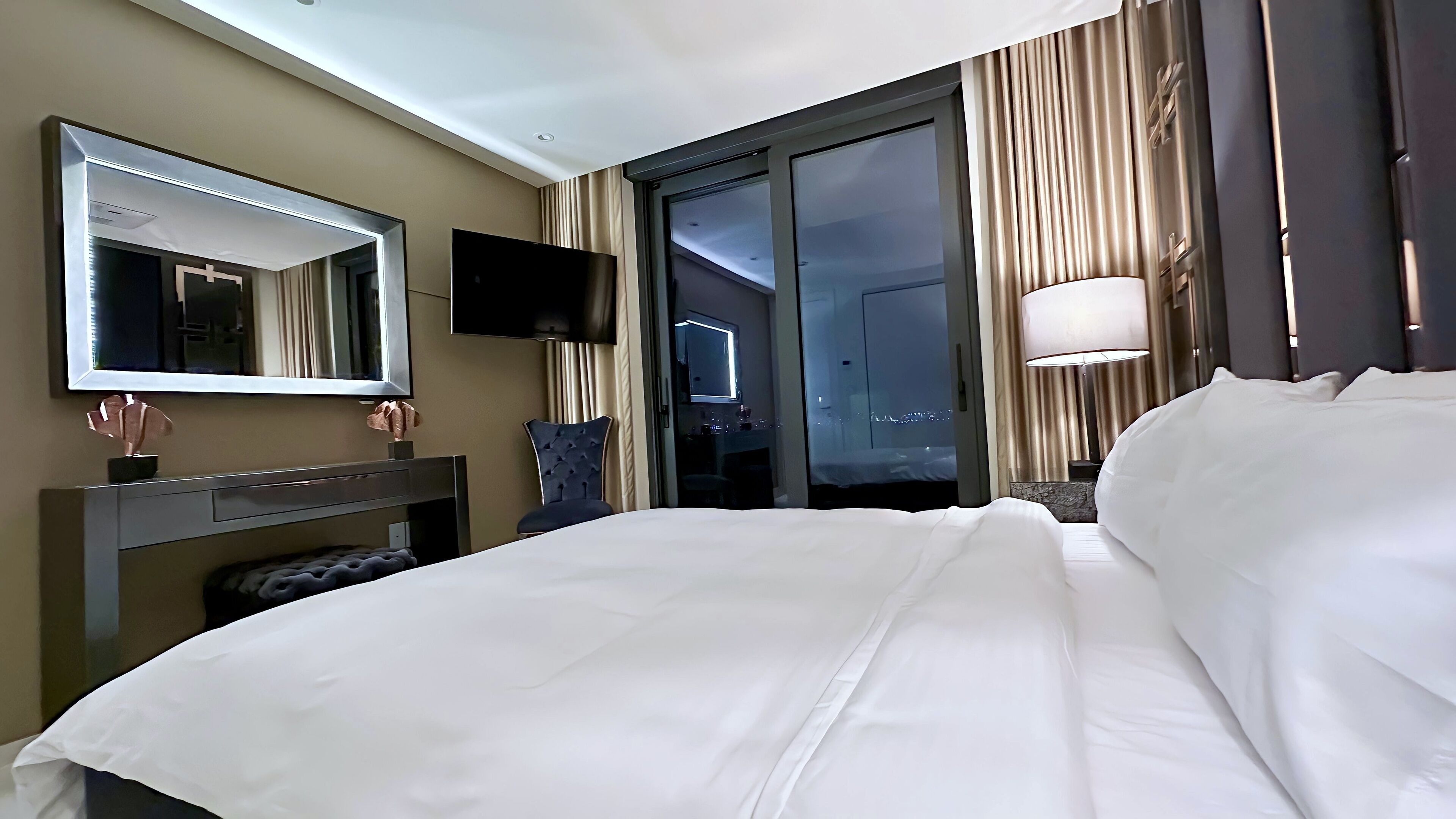 A hotel room with a bed, a TV, a mirror, a desk, and a window with curtains.