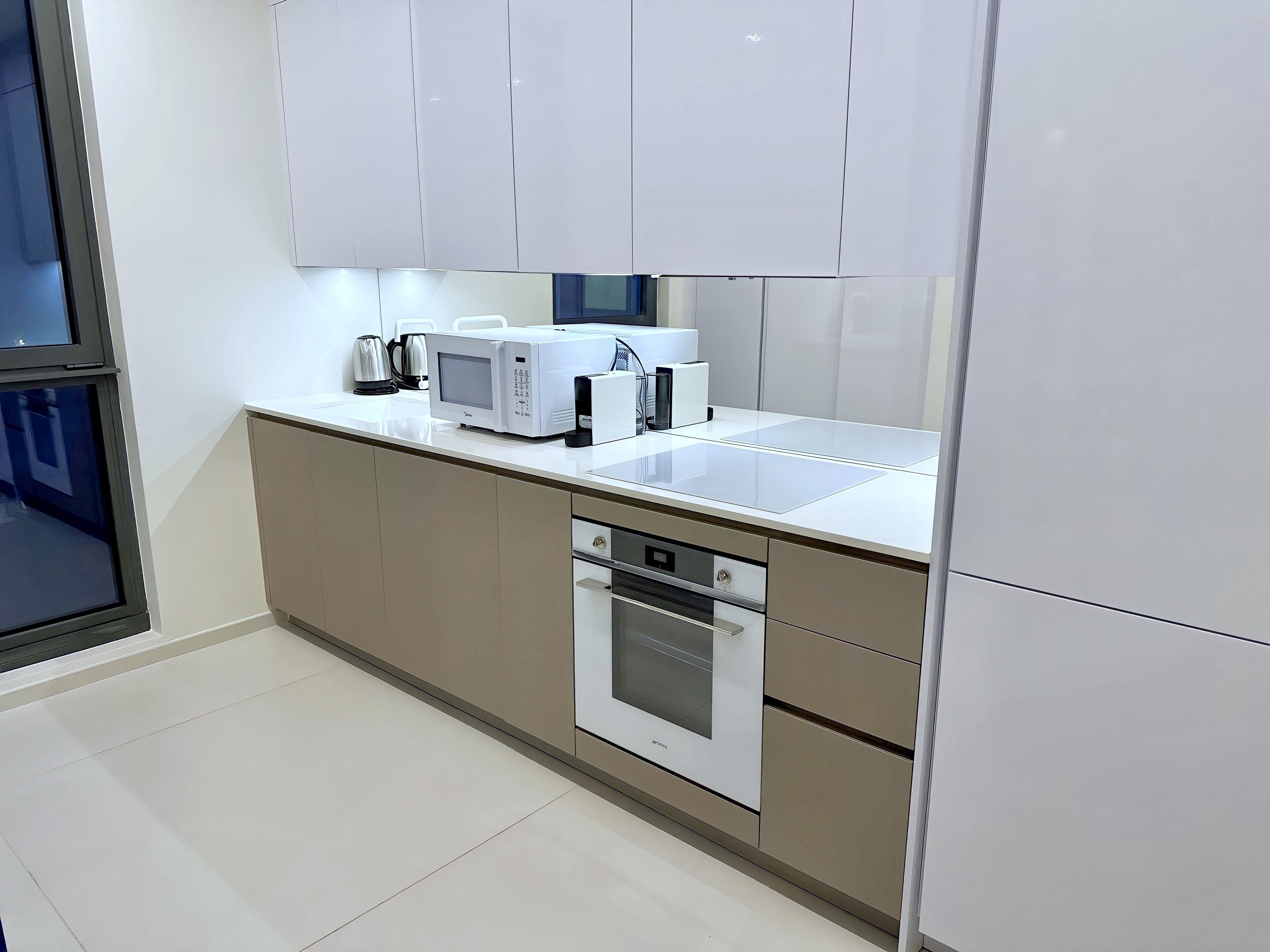 Una cocina moderna con armarios blancos, microondas, cafetera y lavavajillas.