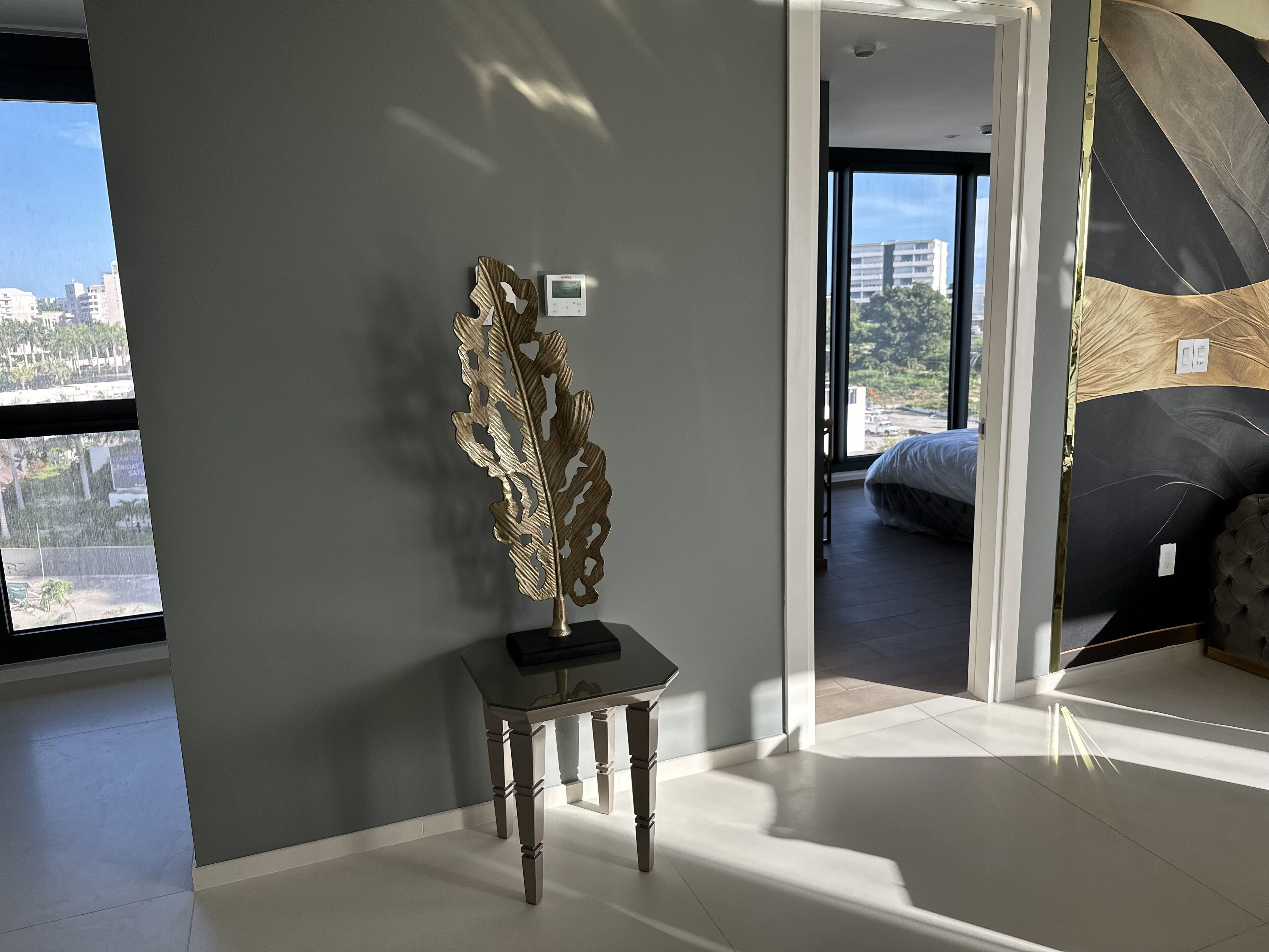 Une chambre moderne avec une grande fenêtre, un élément décoratif mural et un aperçu du lit situé dans la pièce adjacente.