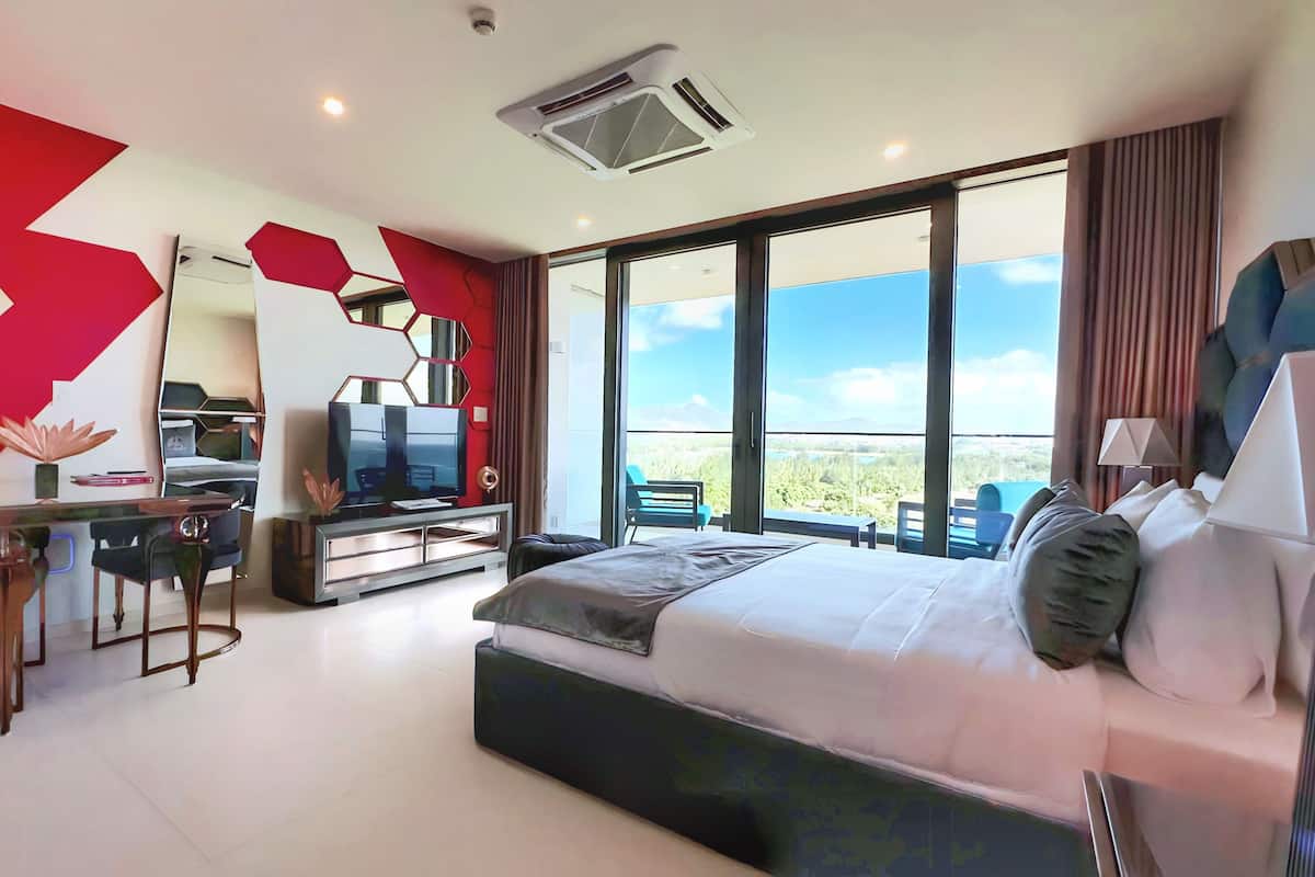 Una habitación de hotel moderna con una cama grande, un escritorio con una silla, un televisor y un balcón con vistas.