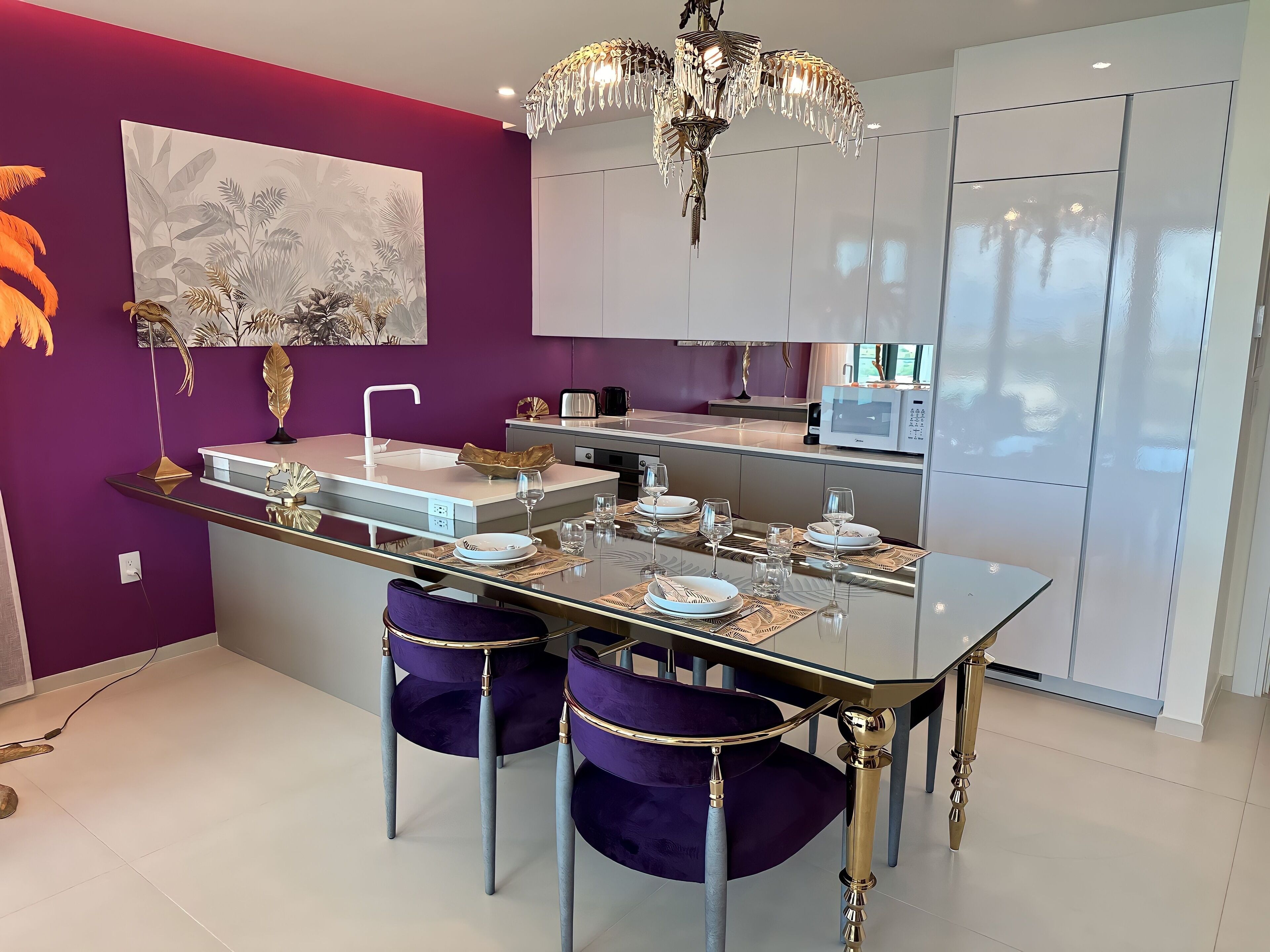 Een moderne keuken met een glazen eettafel, paarse stoelen en een kroonluchter.