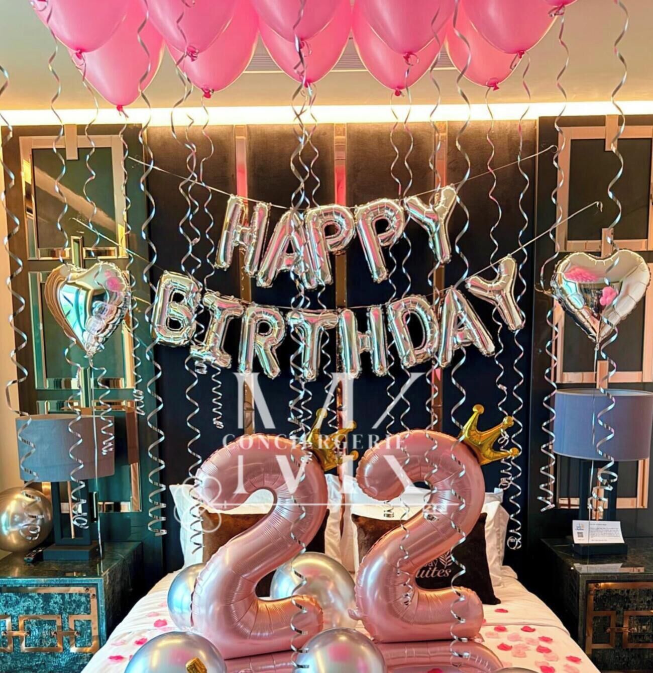 A room with a bed, a mirror, and a wall with a birthday decoration.