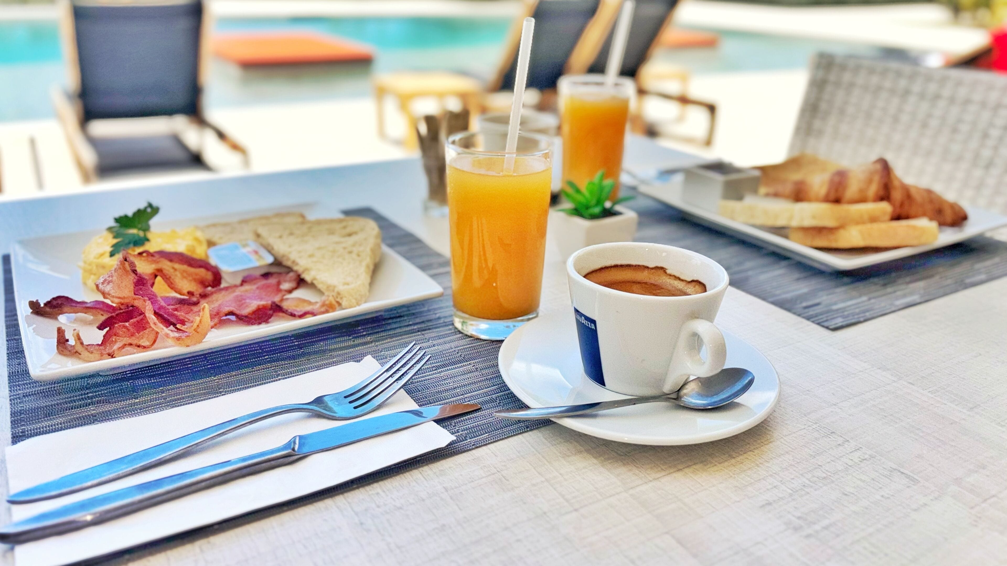 Ein Frühstückstisch mit Toast, Speck, Rührei, einer Tasse Kaffee und einem Glas Orangensaft.