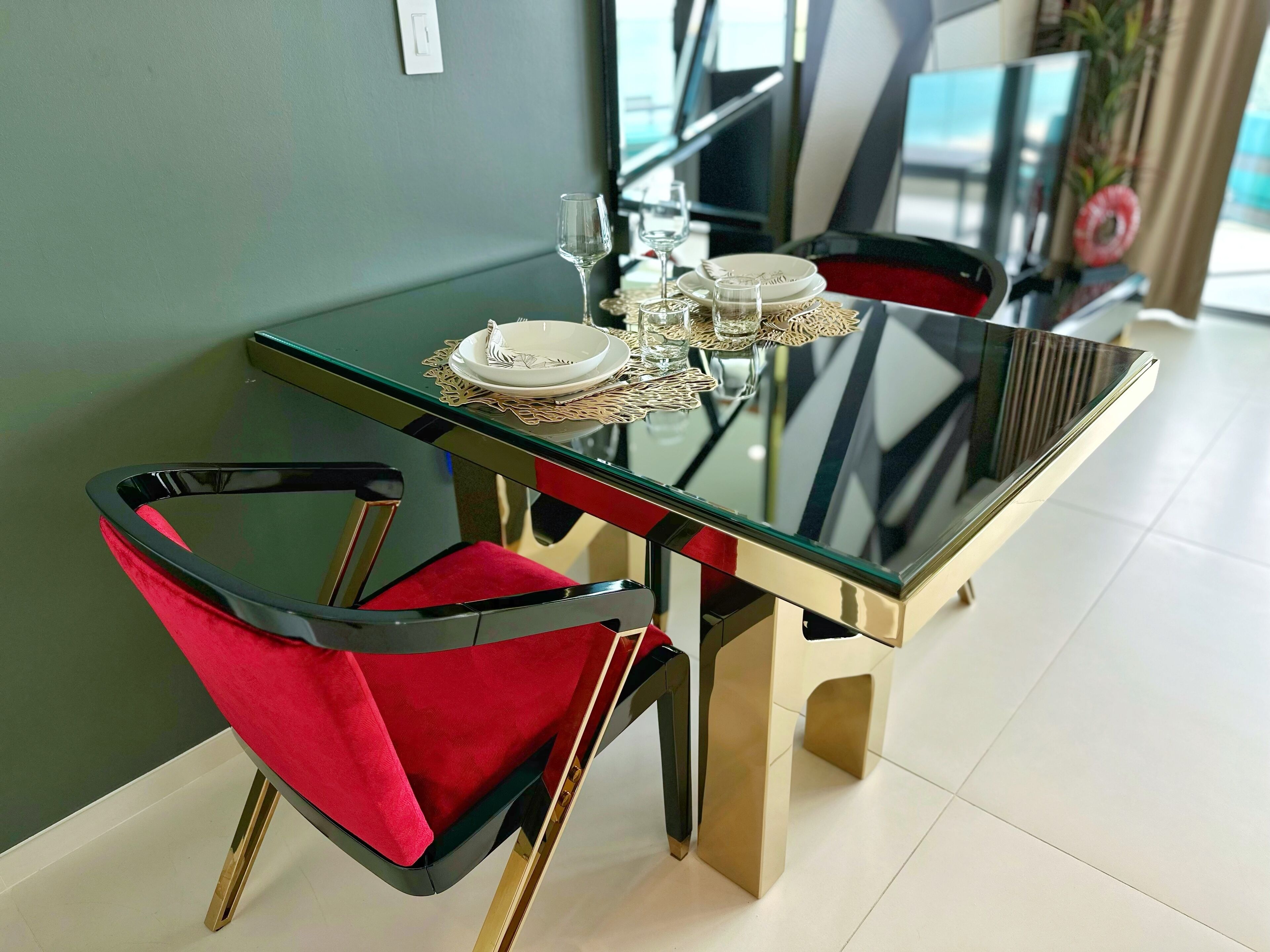 Een eettafel met een glazen blad, omringd door rode stoelen met gouden poten.