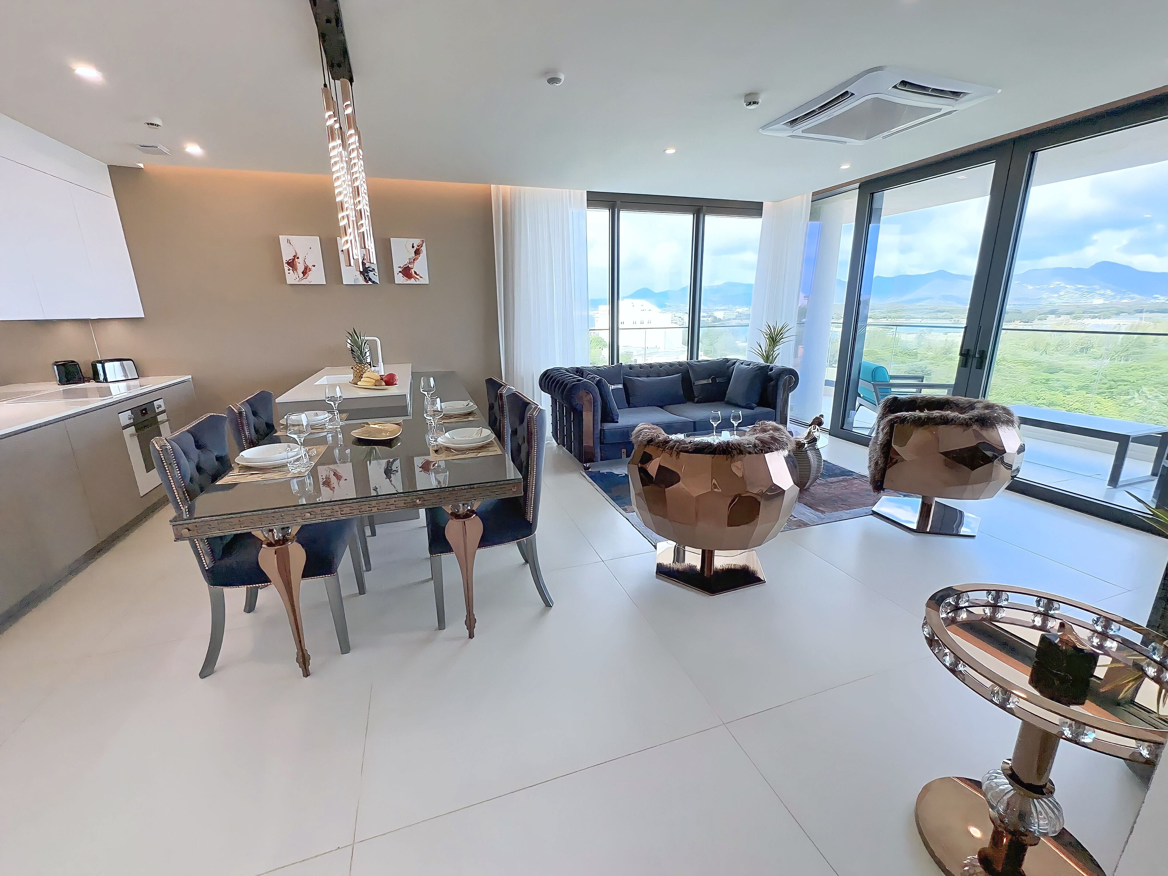Uma zona de refeições moderna com uma mesa de vidro, cadeiras estofadas em azul e vista para o exterior.