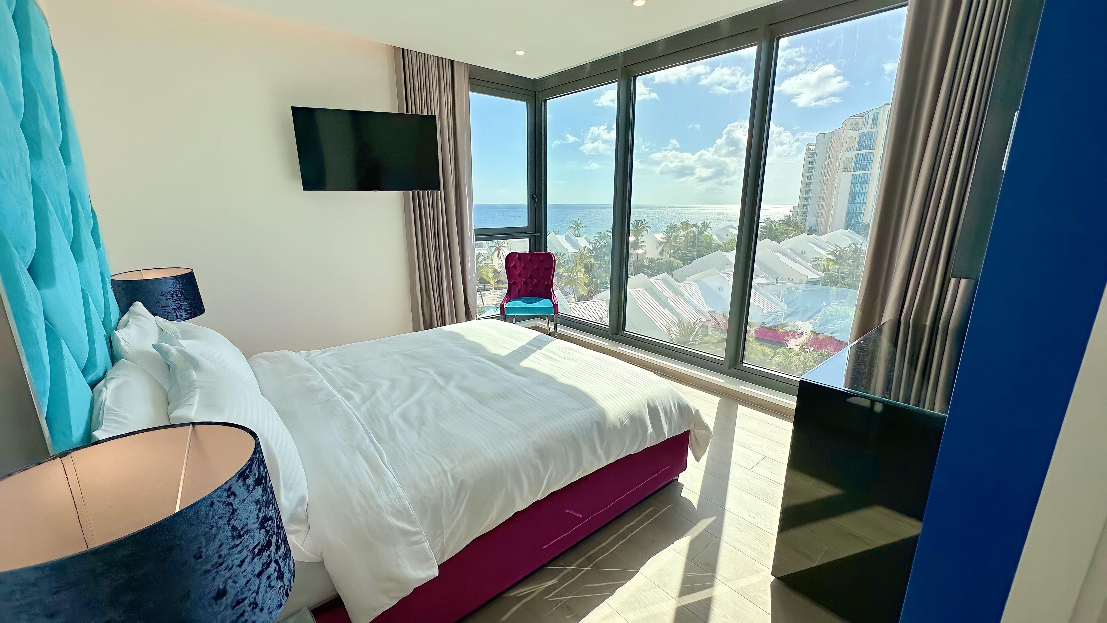 Una habitación de hotel moderna con una cama grande, un televisor de pantalla plana, vista al océano y un balcón con una silla.