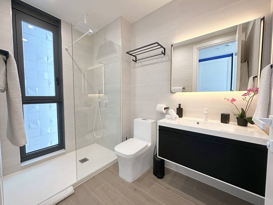 Ein modernes Badezimmer mit einer Duschkabine, Toilette, Waschbecken mit Spiegel und Fenster.