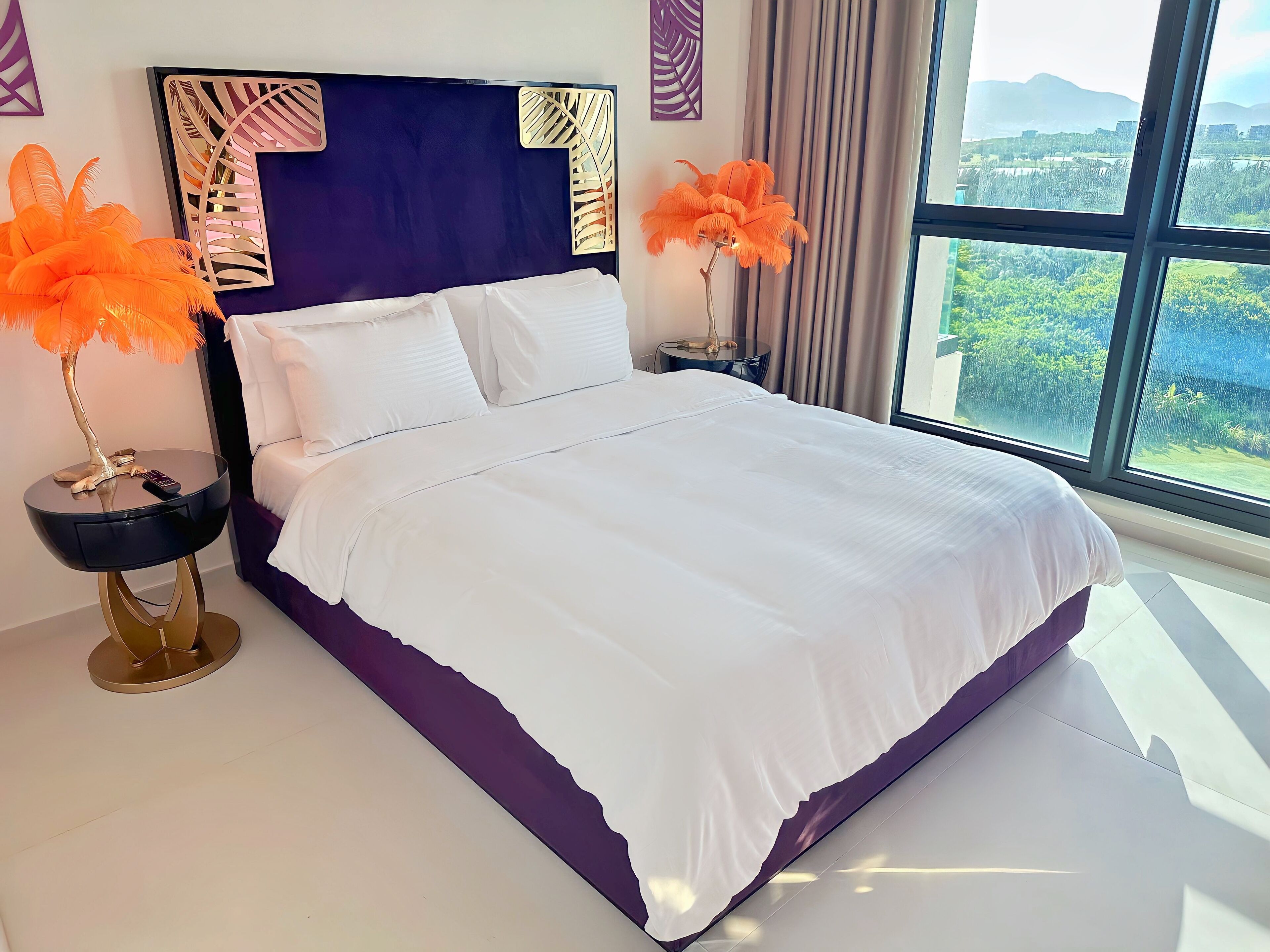 Une chambre moderne avec un grand lit, une vue sur la verdure et des œuvres d’art décoratives au mur.