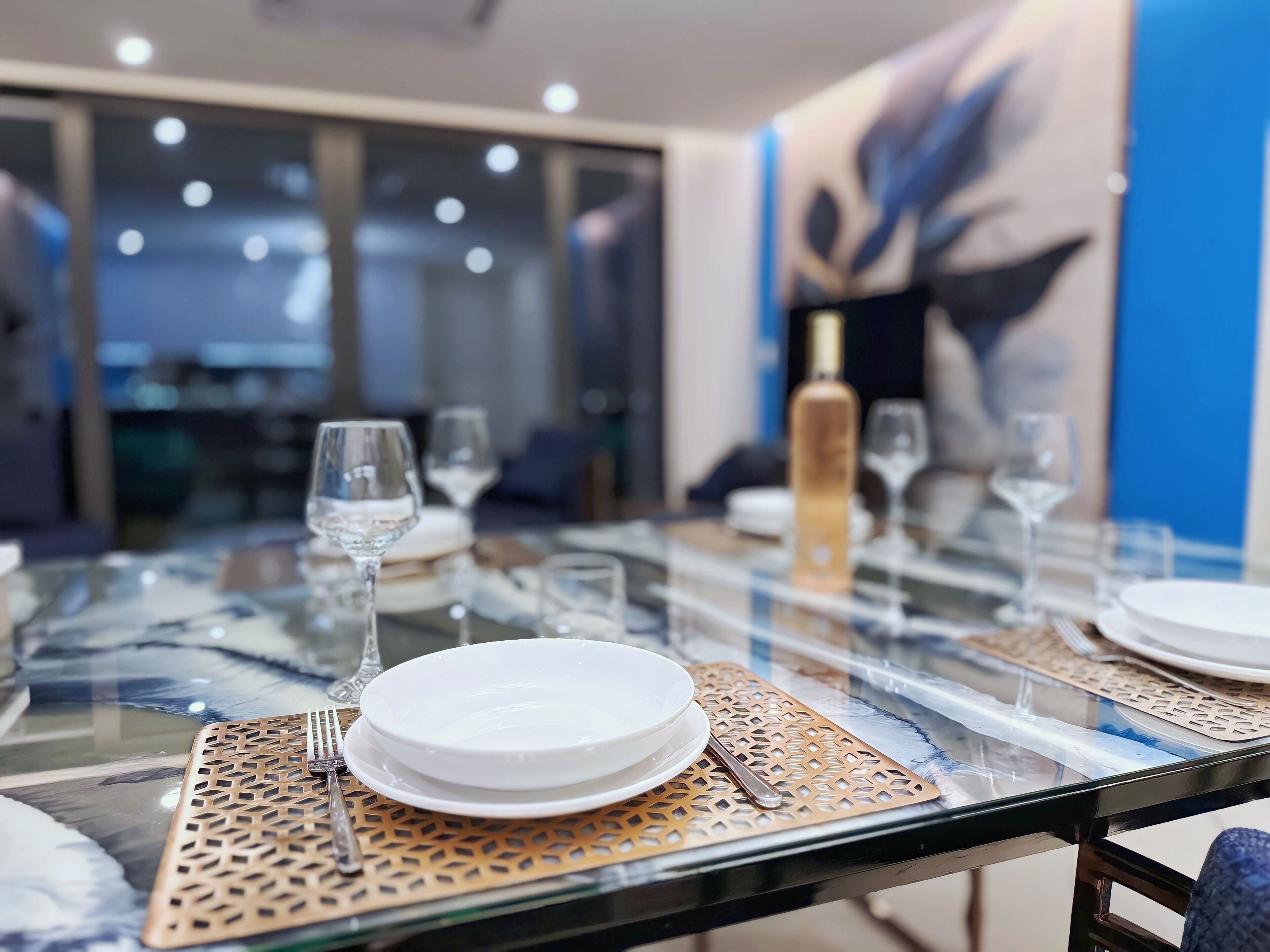 Una mesa de comedor dispuesta con platos, vasos y cubiertos, con un mantel decorativo debajo.