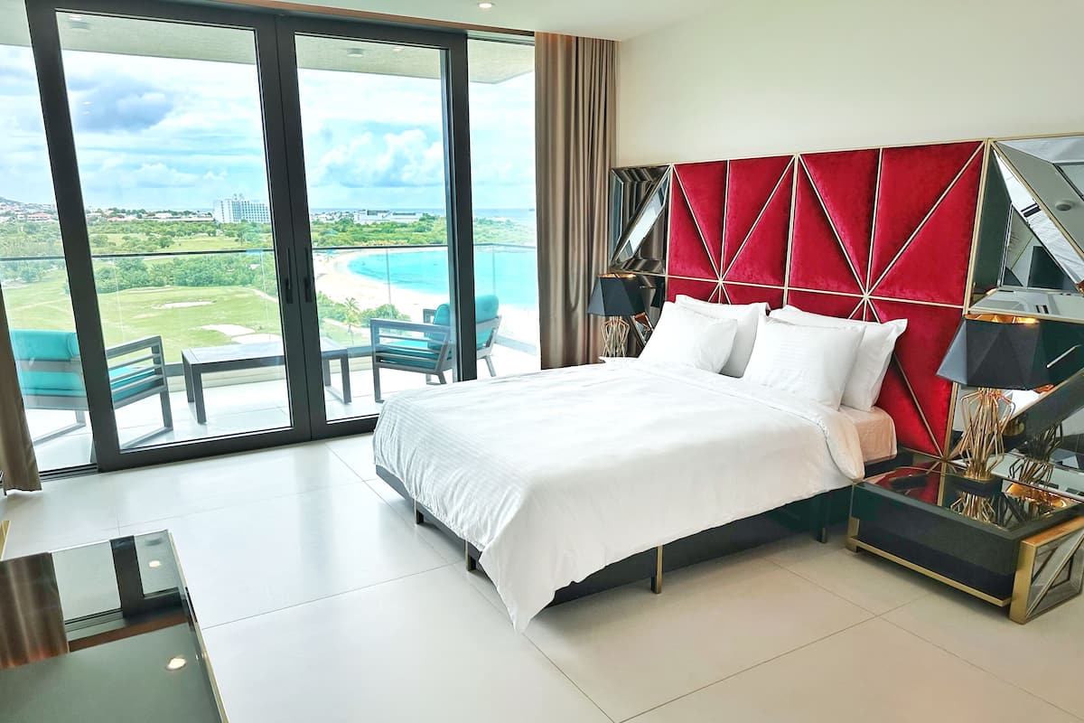 Habitación de hotel moderna con una cama grande, una mesa de vidrio y vistas a una playa y al océano.