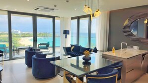 Un saló modern amb taula de vidre, sofàs blaus i vista al mar.