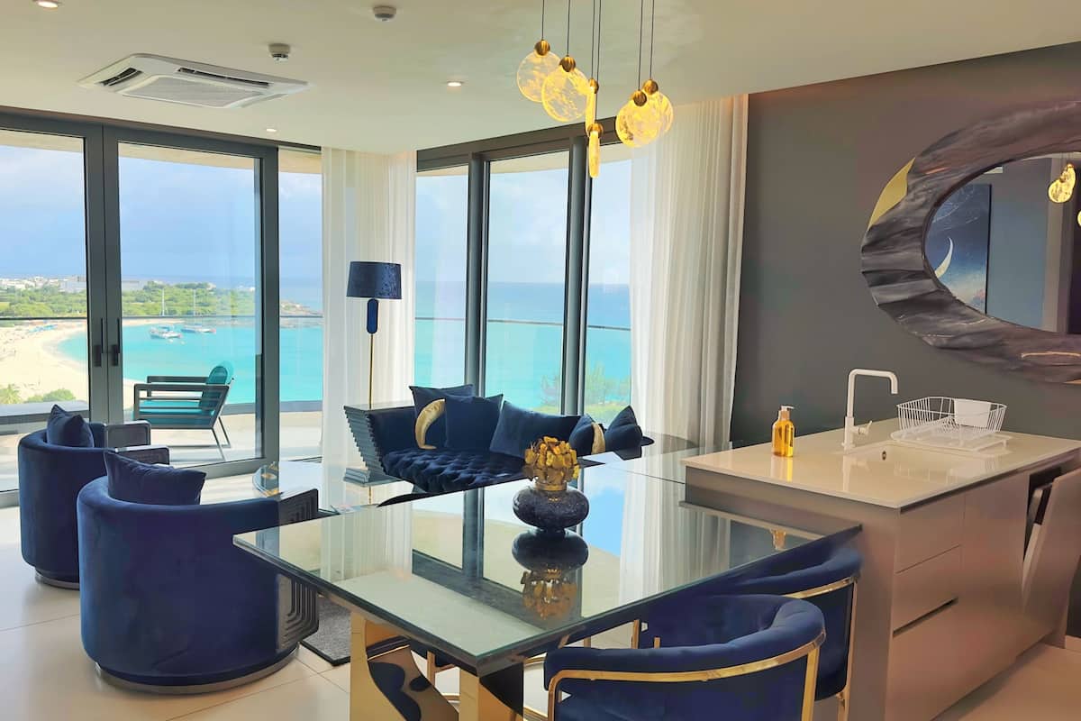 Un salón moderno con una mesa de vidrio, sofás azules y vista al mar.
