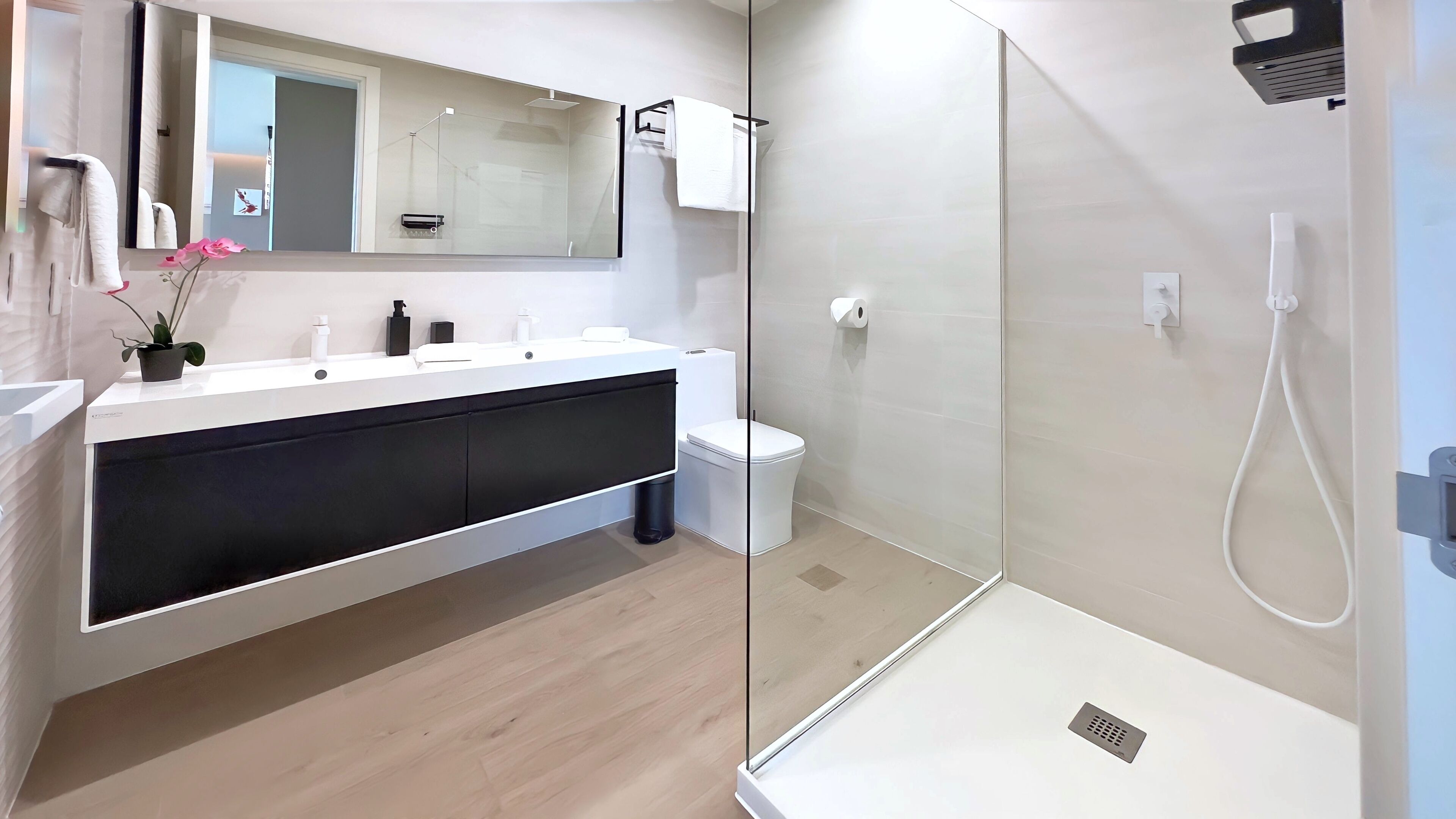 Un bagno moderno con box doccia in vetro, un lavabo bianco con mobiletti neri e un water.