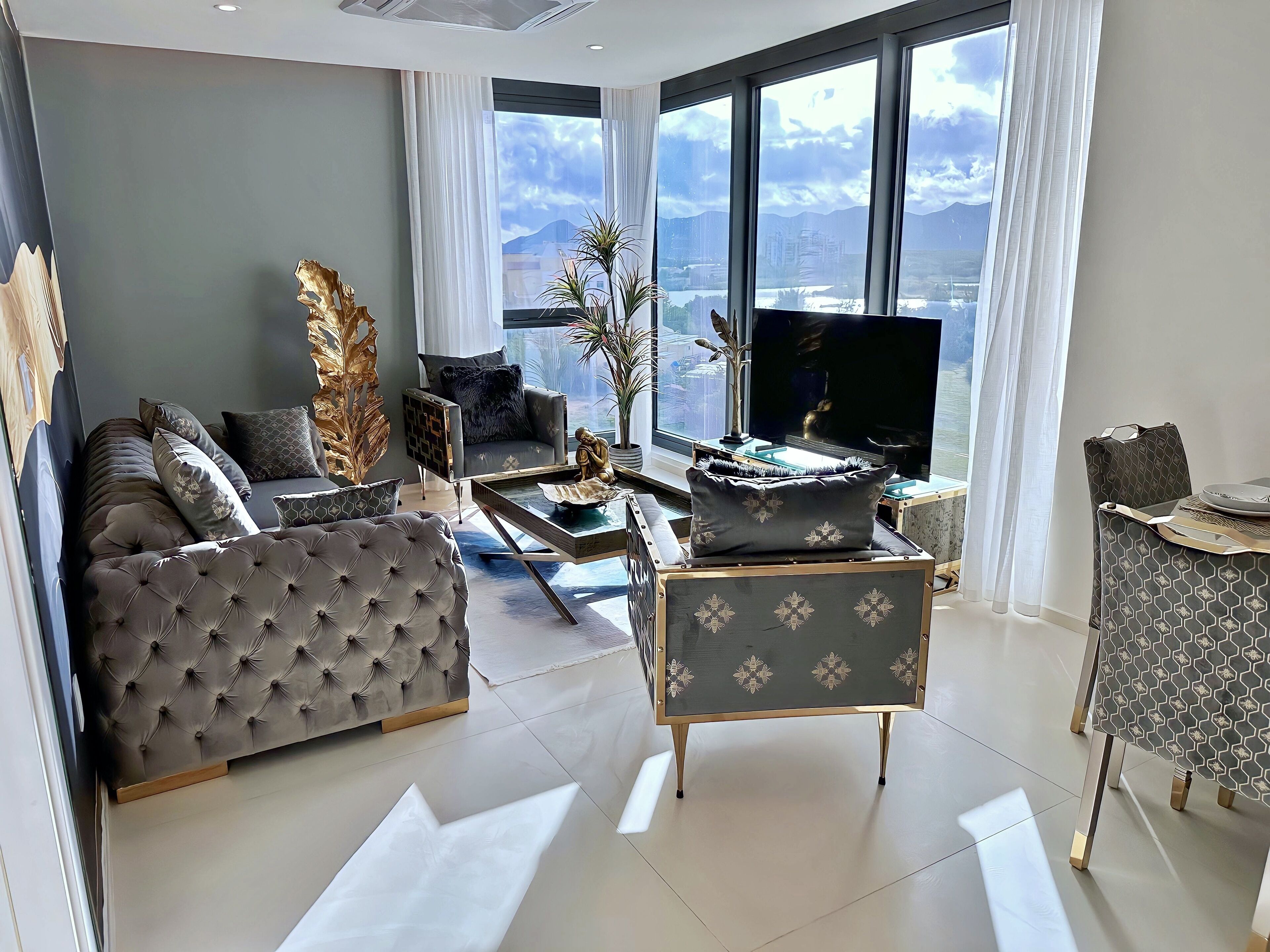 Un salon moderne comprenant un canapé, un fauteuil et une table basse, un téléviseur et une grande fenêtre donnant sur un paysage montagneux.