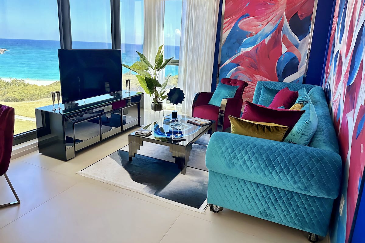 Una sala de estar moderna con un televisor grande, asientos cómodos, una mesa de centro y vista al océano.