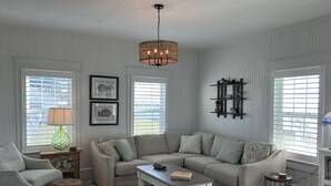 A living room with a sectional sofa, a coffee table, a lamp, and a wall-mounted shelf with decorative items. - Down East Waterfront Quaint Farmhouse with Pier Overlooking National Seashore (Atlantic)