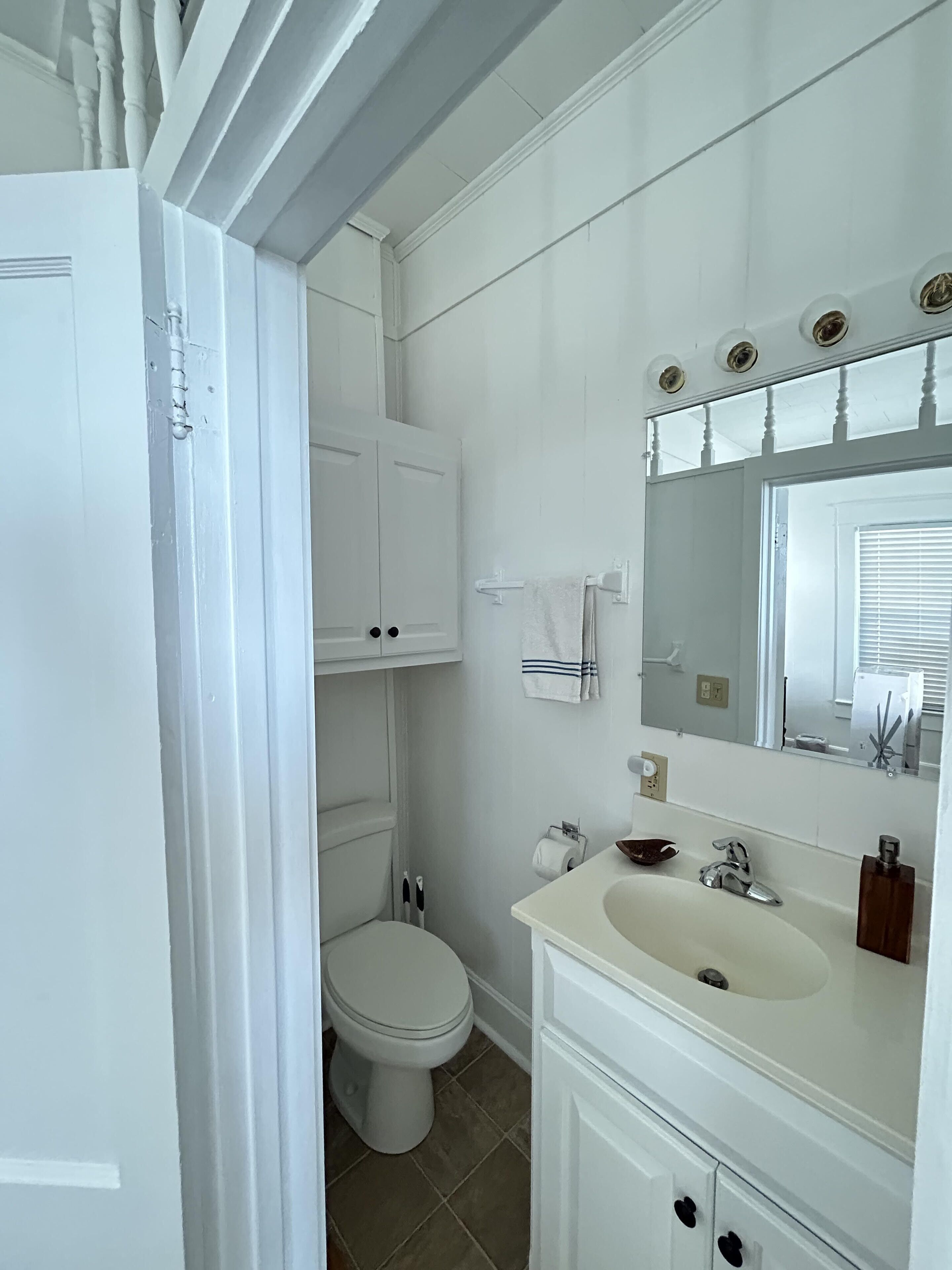 A bathroom with a toilet, sink, mirror, and white cabinets.