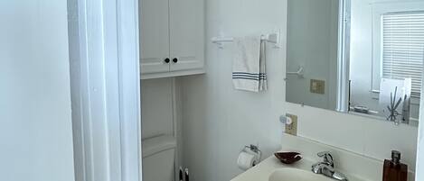 A bathroom with a toilet, sink, mirror, and white cabinets.