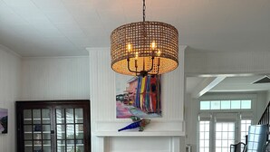 A dining area with a long table, wooden chairs, a hanging light fixture, a fireplace with a colorful painting above it, and a staircase leading to another room. - Down East Waterfront Quaint Farmhouse with Pier Overlooking National Seashore (Atlantic)
