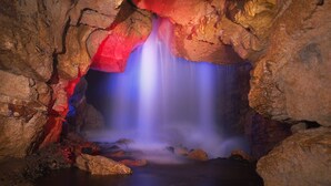 A cave with a blue-lit water feature and rocky walls.
