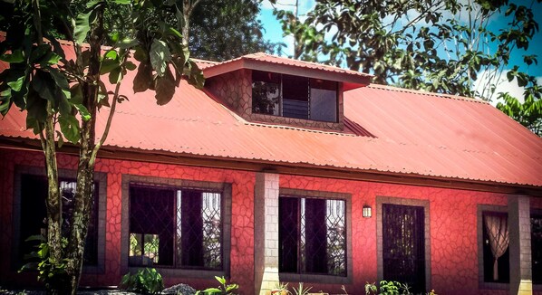 A red building with a sloped roof, large windows, and a small balcony.
