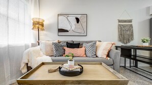 Ein modernes Wohnzimmer mit grauem Sofa, einem Holztisch und einem an der Wand befestigten abstrakten Gemälde.