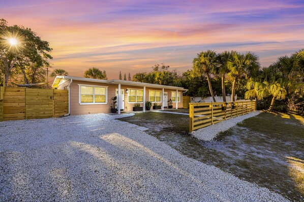 A single-story house with a front porch, a gravel driveway, and a wooden fence.
