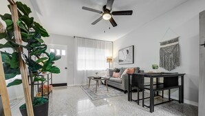 Ein modernes Wohnzimmer mit Deckenventilator, einer Couch, einem Couchtisch und einem Esstisch.