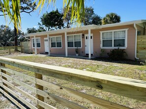 A single-story building with a beige exterior and white trim, featuring a front porch and a small garden area.