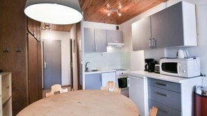 Kompakti keittiö, jossa on modernit kodinkoneet, ruokapöytä ja puupalkit katossa.