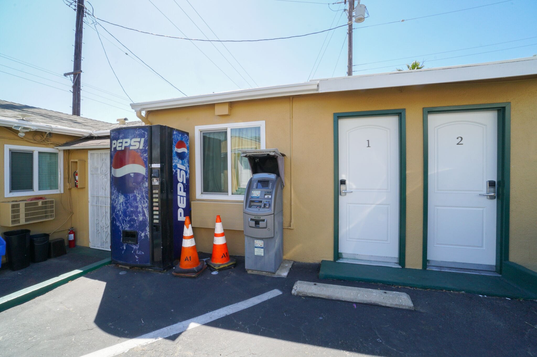 Un pequeño edificio con dos puertas, un estacionamiento, una máquina expendedora de Pepsi y un teléfono público.