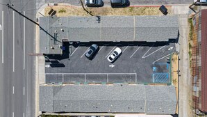 An aerial view of a parking lot with multiple parking spaces, a pedestrian crossing, and a building with a red roof in the background.