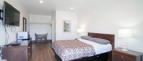 A bedroom with a bed, bedside tables, a desk, a chair, a TV, and a picture on the wall.