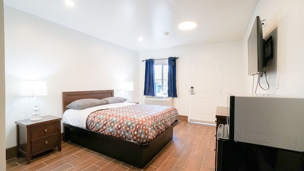 A bedroom with a bed, nightstands, a TV, and a window with curtains.