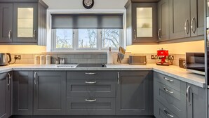 A modern kitchen with dark cabinets, a window with a view, and a clock on the wall. - 2 bedroom accommodation in Falfield, near Wotton-under-edge (Falfield, near Wotton-under-edge)