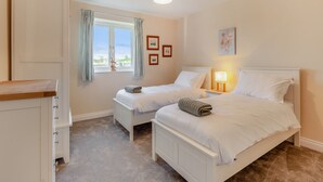 A bedroom with two beds, a window with curtains, a bedside table with a lamp, and a wardrobe. - 2 bedroom accommodation in Falfield, near Wotton-under-edge (Falfield, near Wotton-under-edge)