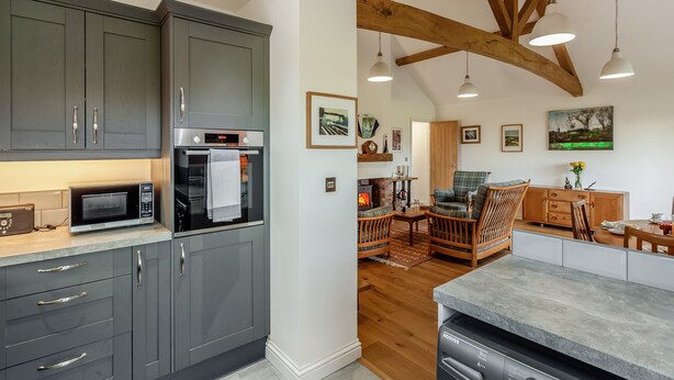 A modern kitchen with grey cabinets, a built-in oven, and a microwave. There is a dining area with wooden furniture and a fireplace. - 2 bedroom accommodation in Falfield, near Wotton-under-edge (Falfield, near Wotton-under-edge)
