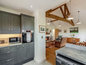 A modern kitchen with grey cabinets, a built-in oven, and a microwave. There is a dining area with wooden furniture and a fireplace.