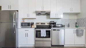 Een moderne keuken met roestvrijstalen apparatuur, witte kasten en een betegelde achterwand.