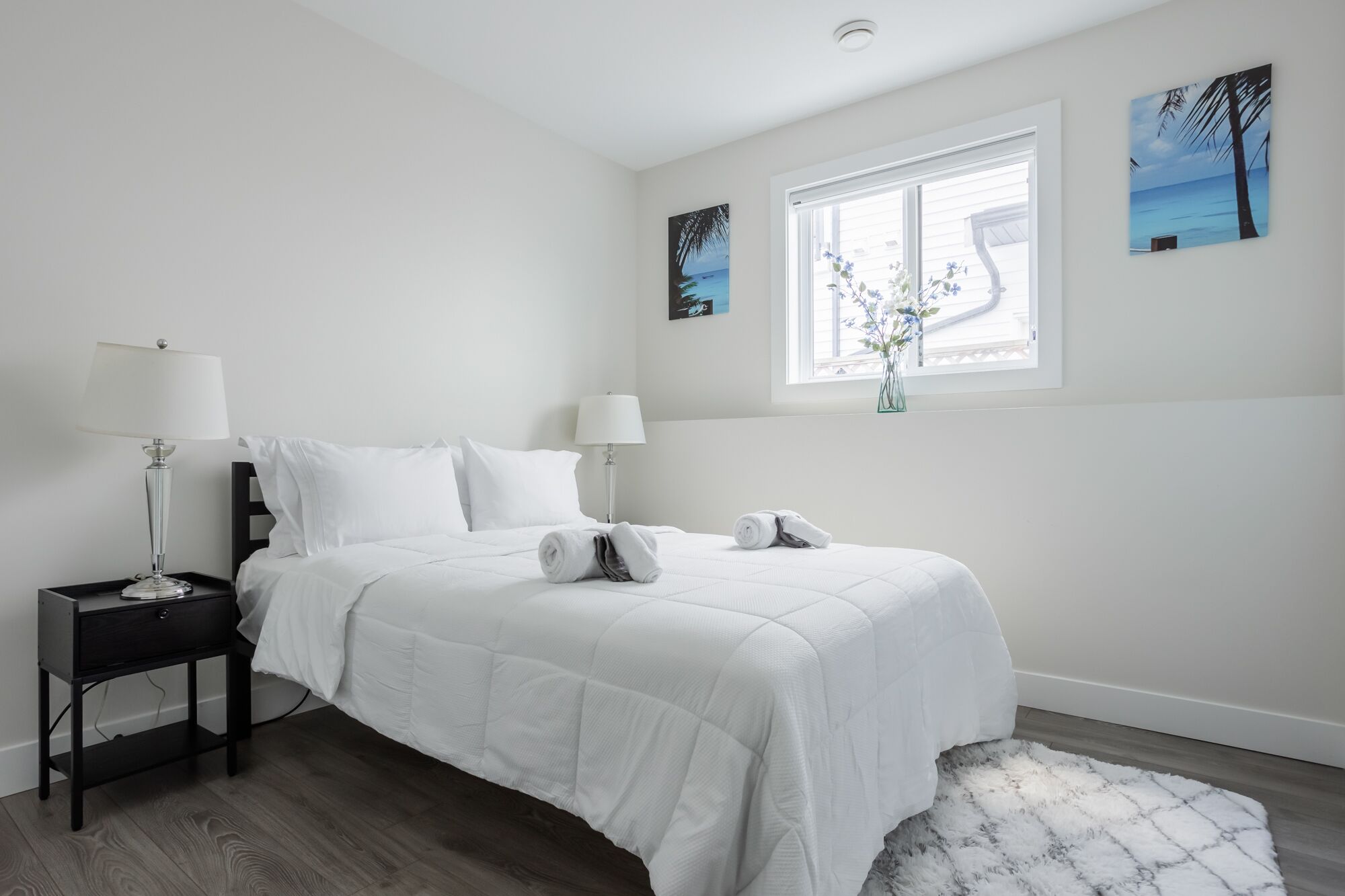 A minimalist bedroom with a bed, bedside tables, and artwork on the walls.