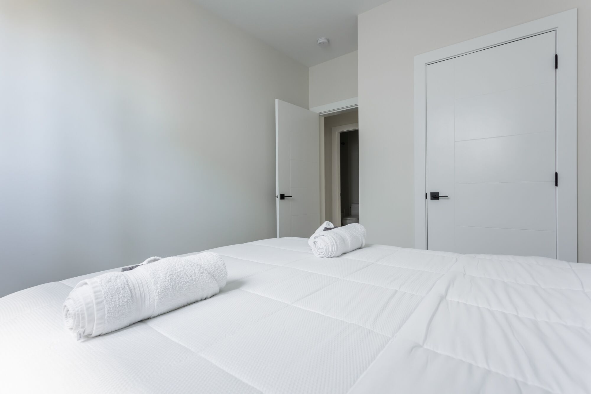 Een hotelkamer met een groot bed, twee witte deuren en uitzicht op de badkamer.
