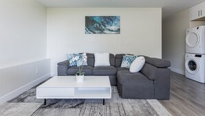 Een moderne woonkamer met een grijze hoekbank, een witte salontafel en een groot abstract schilderij aan de muur.