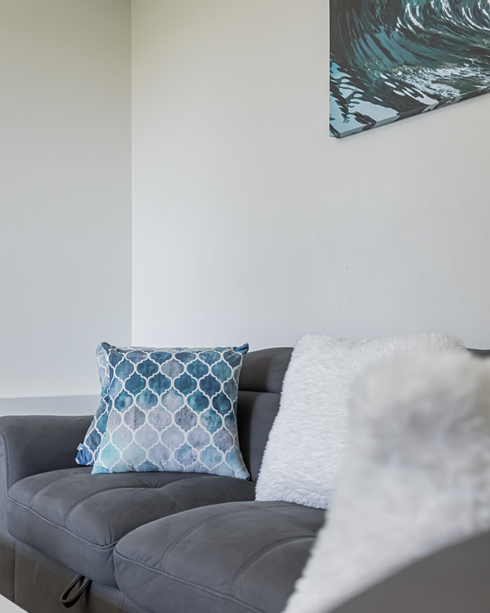 Un sofá gris con un cojín estampado y una manta suave color blanco.