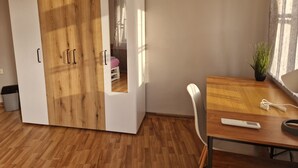 Una habitación con un armario de madera, una mesita con una planta y una silla.