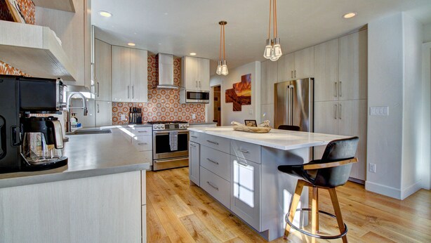 A modern kitchen with a large island, stainless steel appliances, and a wooden floor.