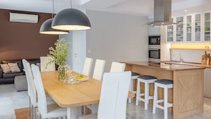 Een moderne keuken met witte kasten, een centraal eiland met krukken, en een eetgedeelte met een houten tafel en witte stoelen.