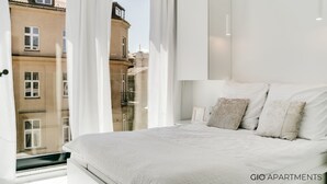 A modern bedroom with a large bed, white bedding, and a view of buildings through sheer curtains. - Luxury Apt • Balcony View • 5 min to Downtown (Kraków)