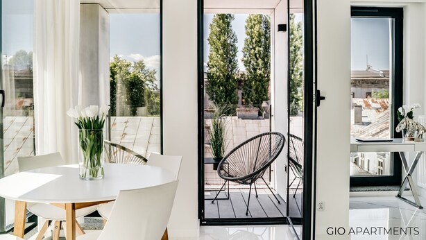 A modern apartment with a balcony, a dining area with a table and chairs, and a view of trees and buildings. - Luxury Apt • Balcony View • 5 min to Downtown (Kraków)