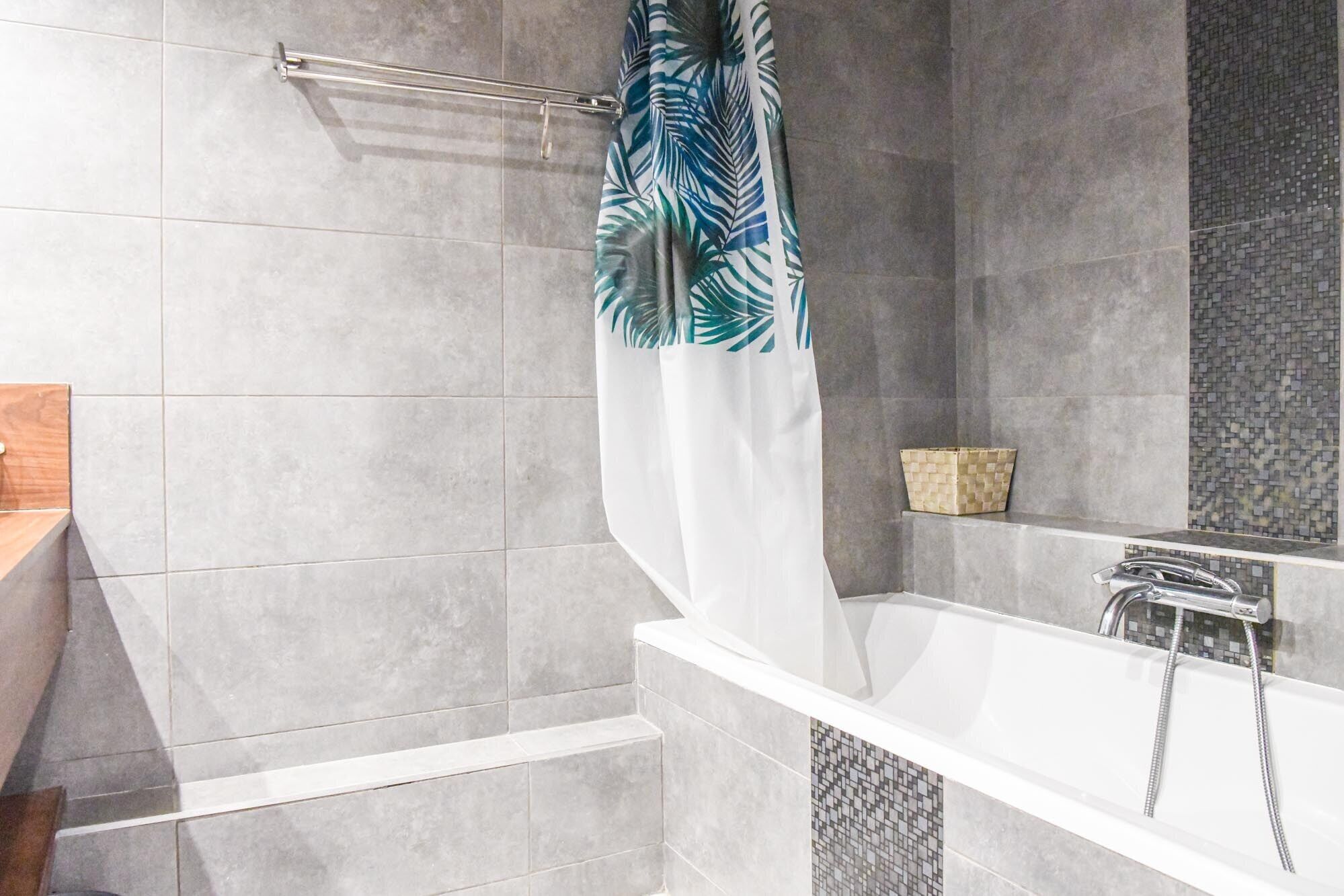 Ein modernes Badezimmer mit einer Badewanne, einer Duschvorhang mit Blättermotiv und einer gefliesten Wand.